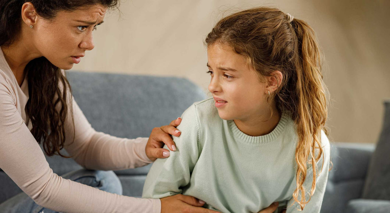 A distressed child holds her stomach while her concerned mother examines her.