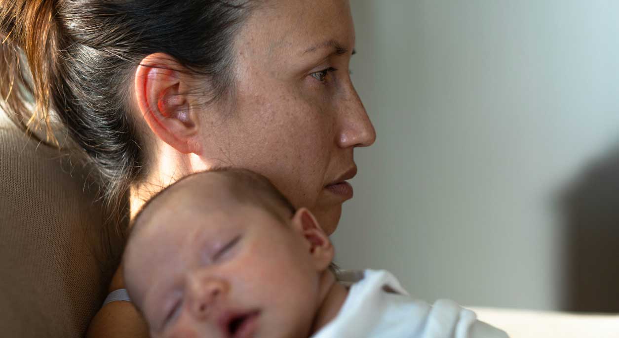 A new mother with her baby asleep on her shoulder experiences baby blues symptoms.