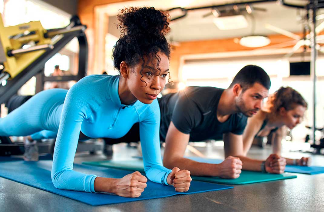 Three athletes doing a planking exercise in a gym.