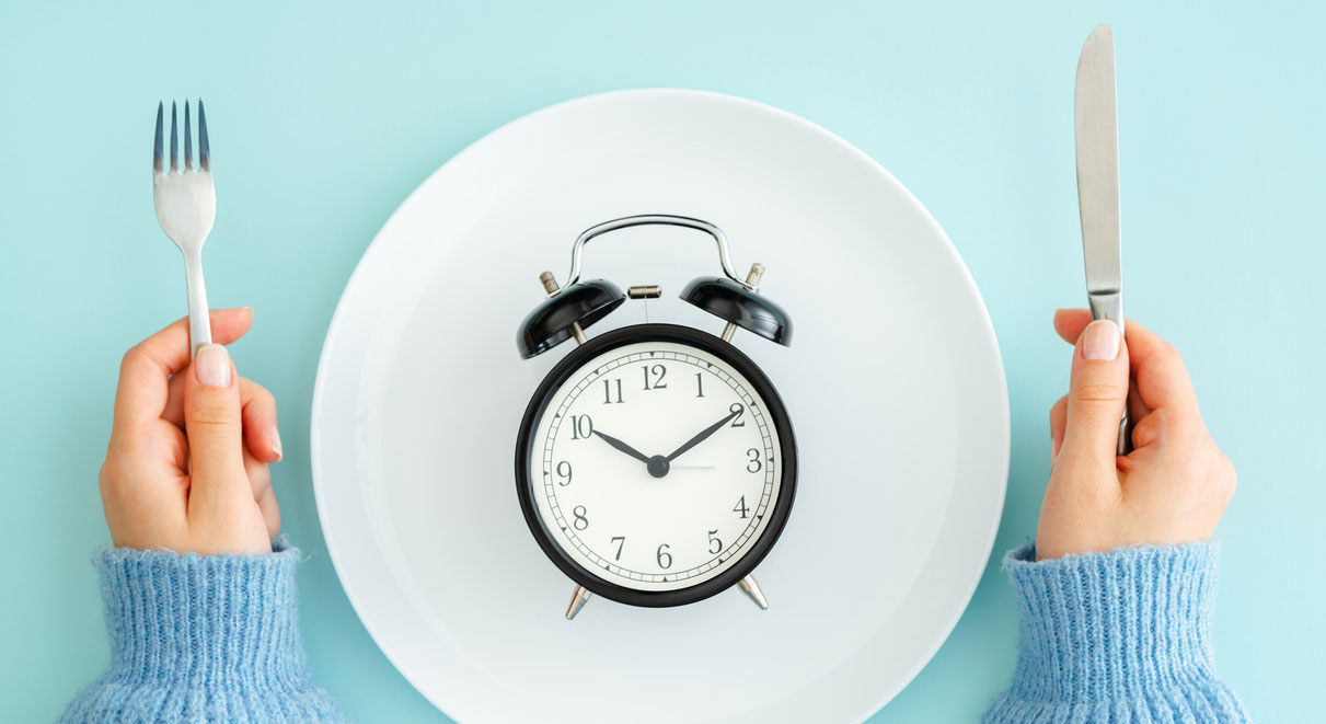 A clock on a dinner plate, with a woman's hands holding a fork and knife on either side.