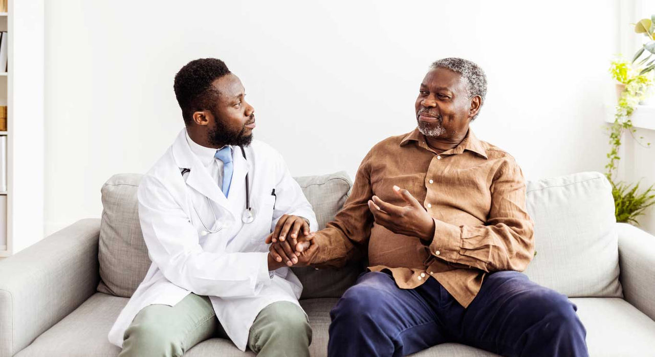 A young doctor sitting and talking with an older patient.
