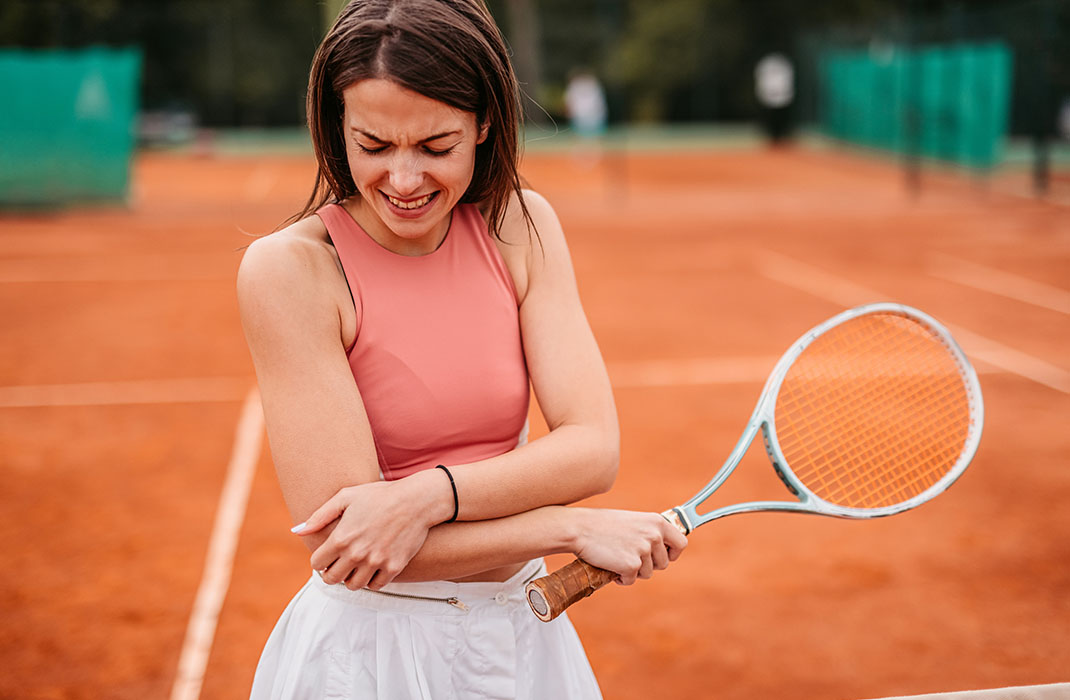 woman holding tennis racket grabbing her elbow in pain 