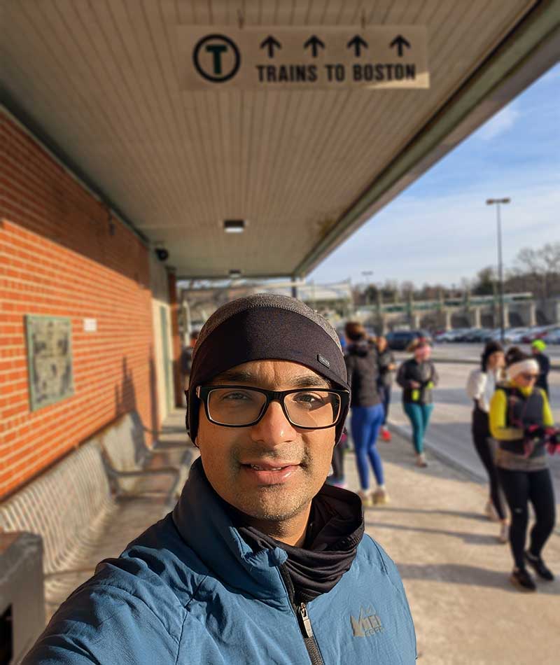 Ipsit Vahia outside a Boston subway station, with a sign above him reading Trains to Boston.