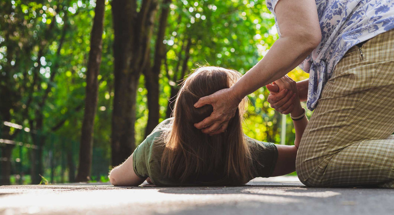 Woman lying on the ground with another person holding her head off the ground and holding her hand.