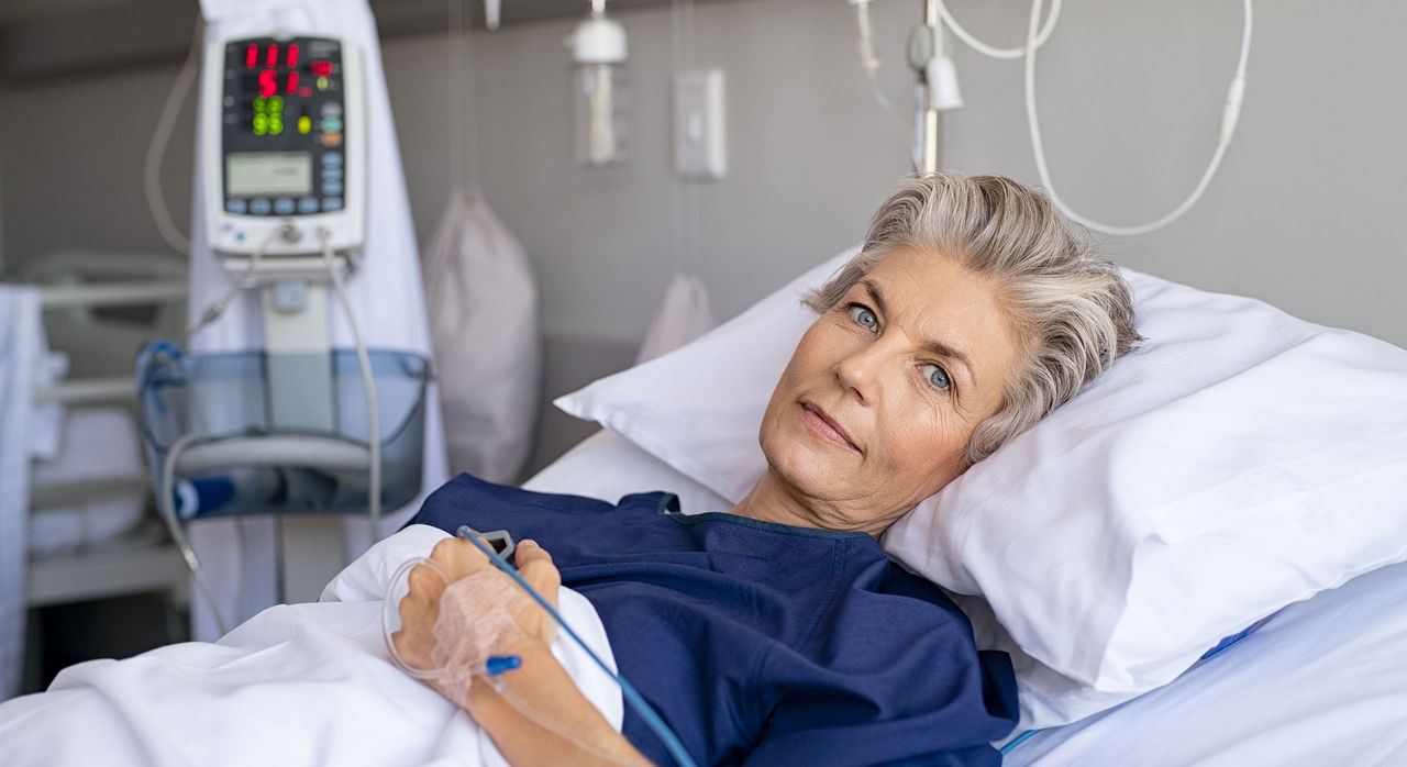 An older woman in a hospital bed, hooked up to an IV.