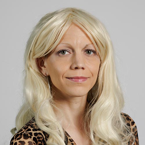 A person with long, wavy blonde hair is shown in front of a plain and neutral background.