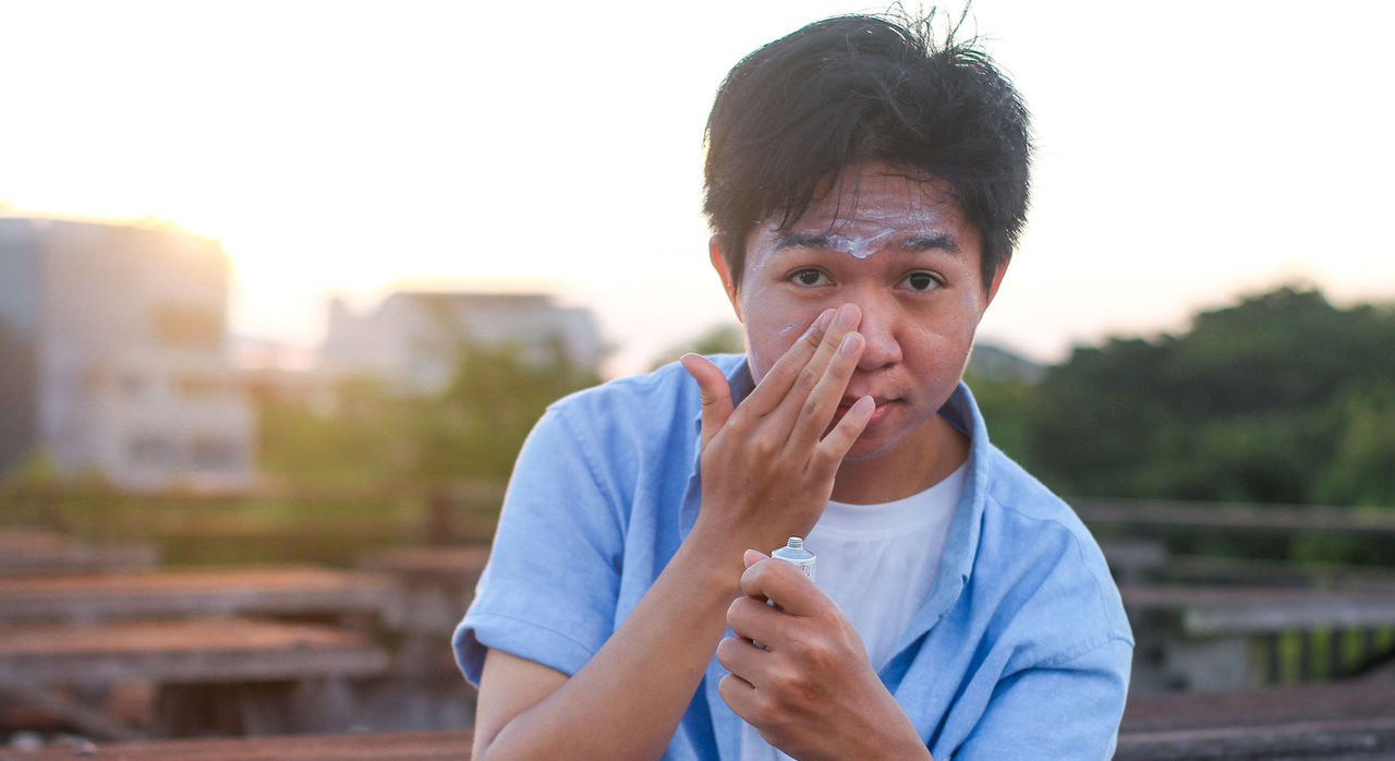 Young man applies sunscreen to face