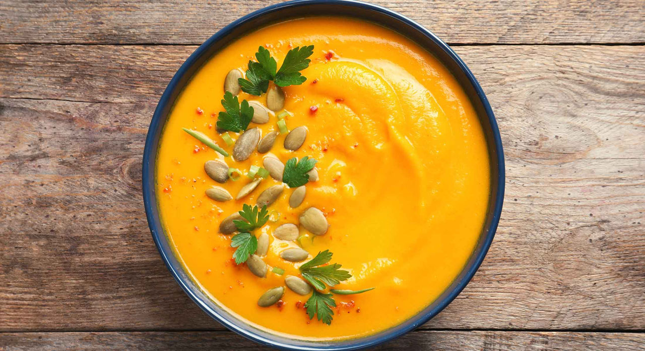 Top view of a delicious pumpkin cream soup in bowl on wooden background