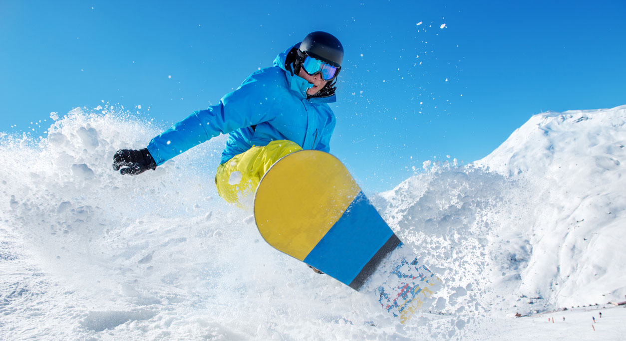 A snowboarder performs an explosive jump through snow on a mountain.