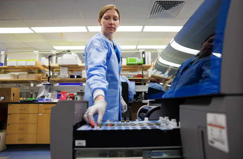 A lab scientist loads vials into a piece of equipment, which looks a lot like a filing cabinet drawer.