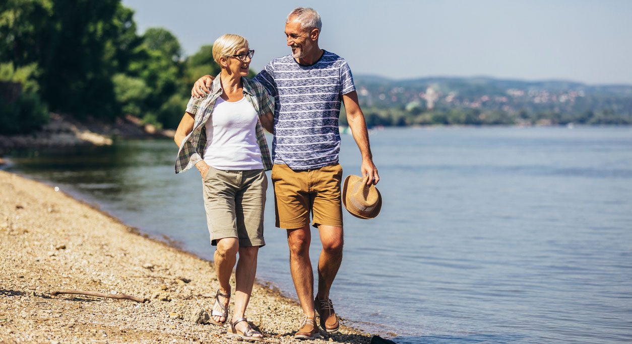 A happy older couple walk along the beach together in summertime.