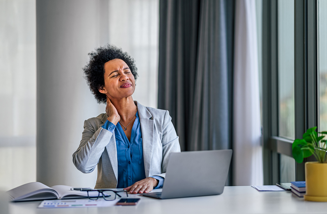 businesswoman at office desk holding sore neck