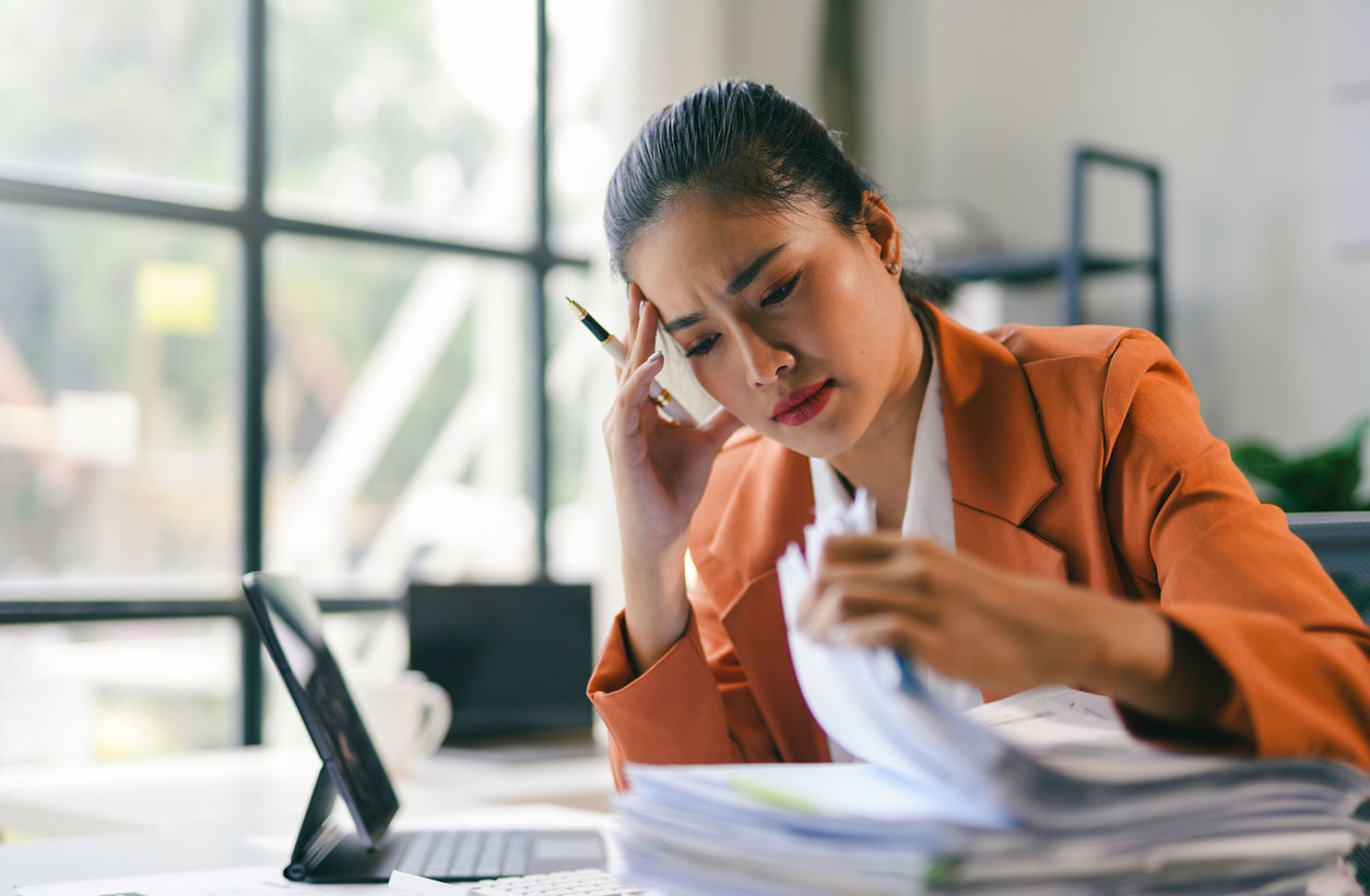 A stressed-looking businesswoman flips through the tall stack of papers on her desk.