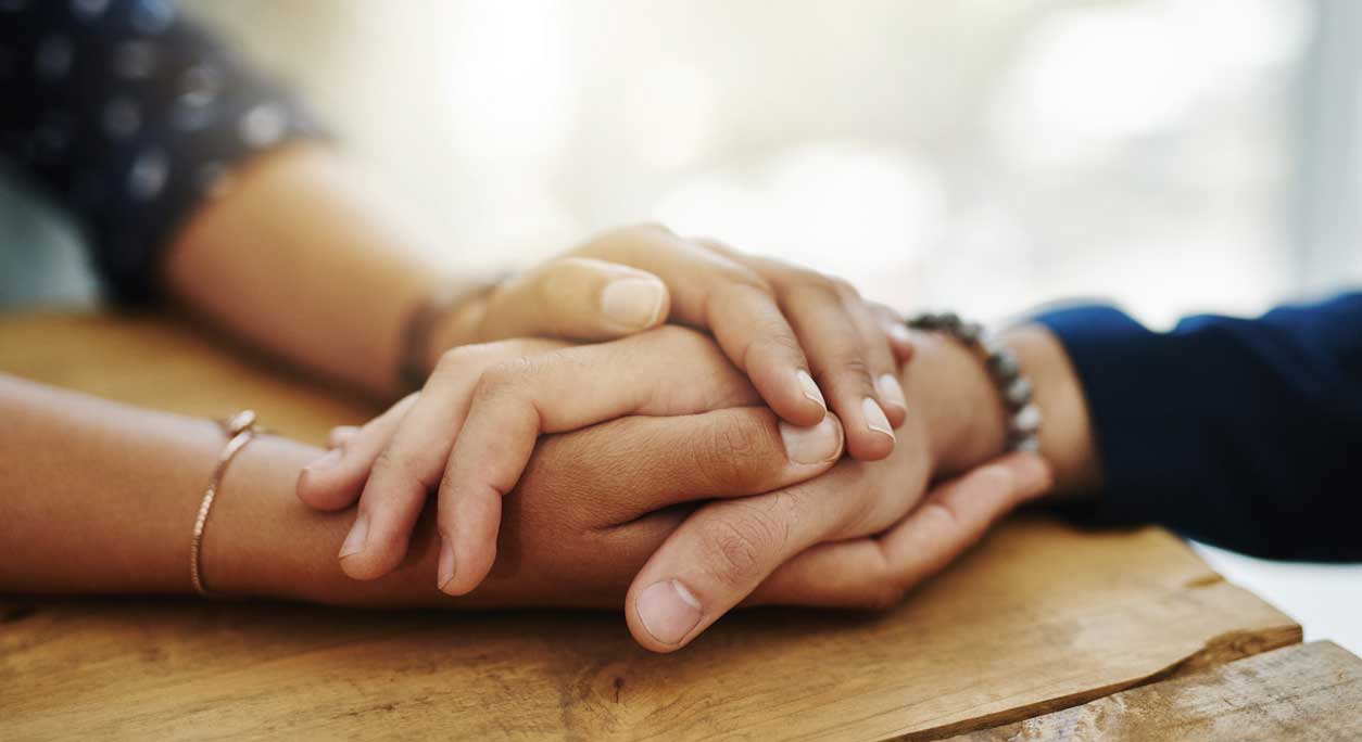 A woman clasps a friend's hand comfortingly.