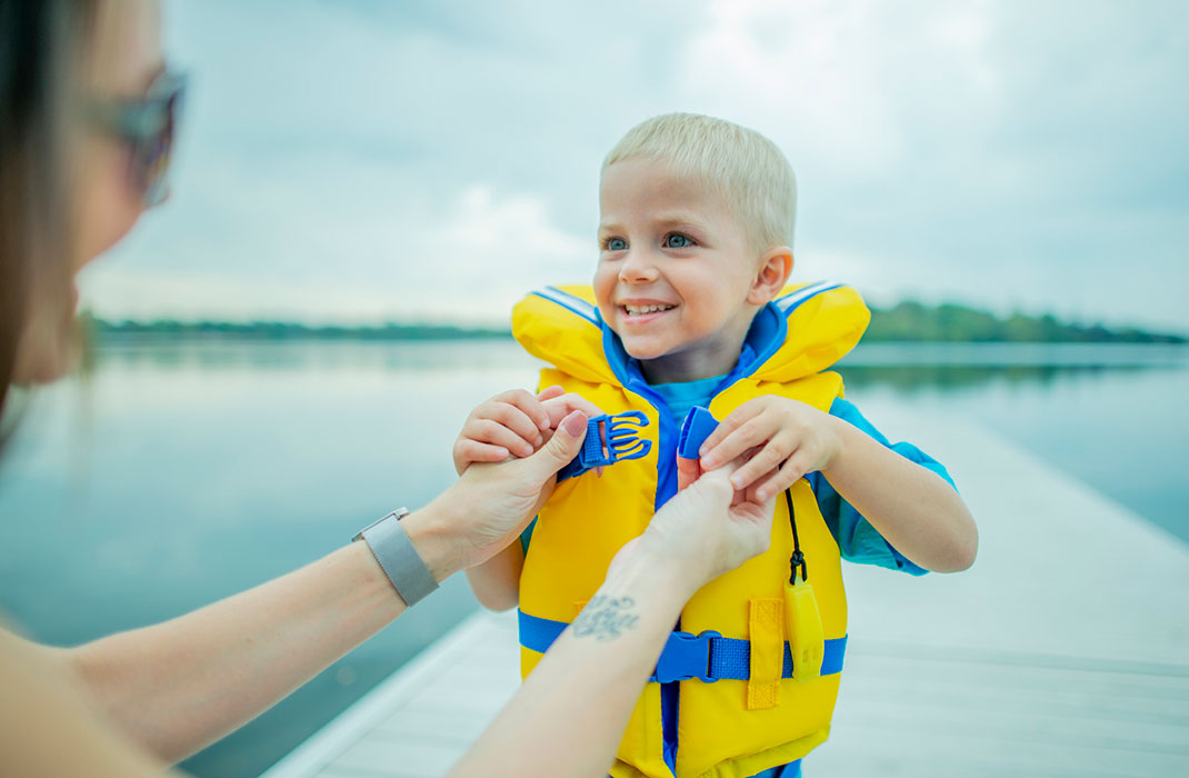 A woman does up a small boy's life vest at the lakeside.