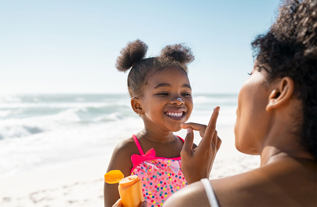 A mother puts sunscreen on her small daughter at the beach.