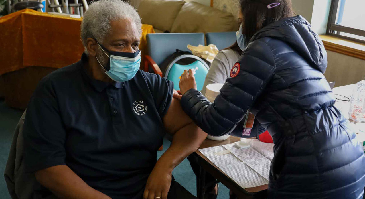 Elderly masked individual receiving a vaccine administered by a healthcare worker