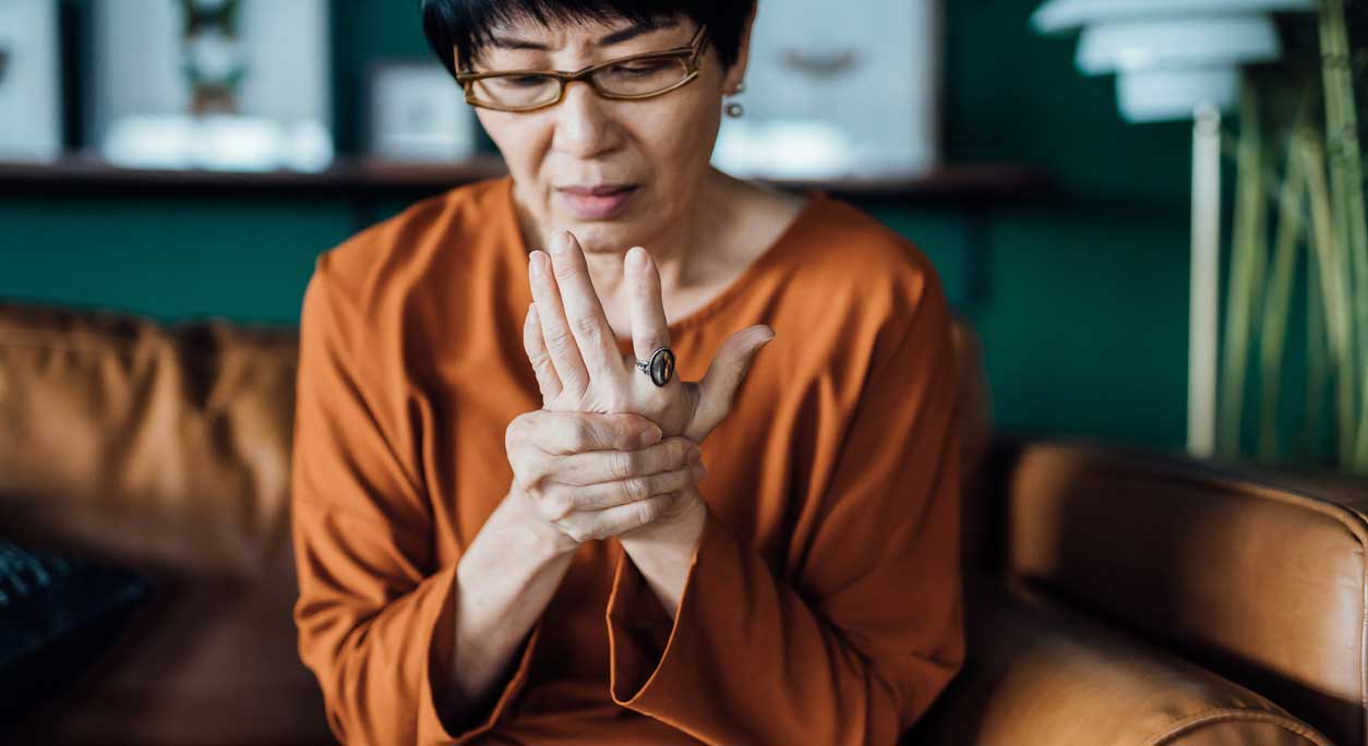 A woman with rheumatoid arthritis rubbing her hand in discomfort.