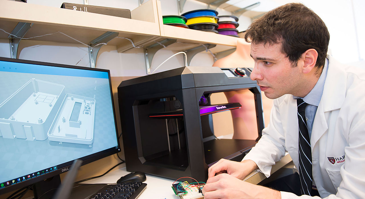 Researcher looks at a 3D rendering on the computer while adjusting a prototype