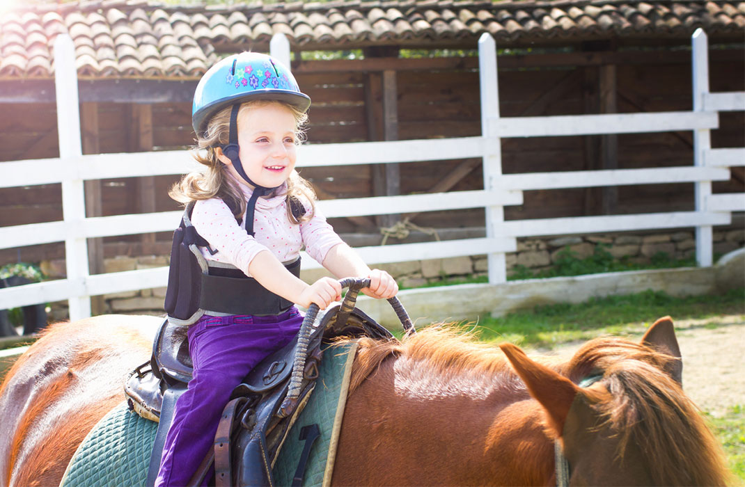 Little girl holding onto saddle during therapeutic horseback riding lesson.