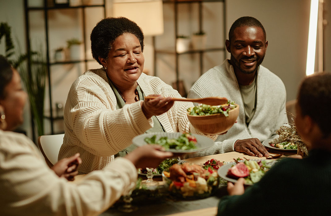Portrait of smiling African-American grandmother serving food while celebrating Thanksgiving with big happy family at dinner table