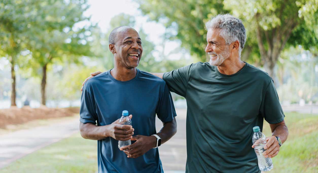 Two older men walking outside with water bottles, laughing together.