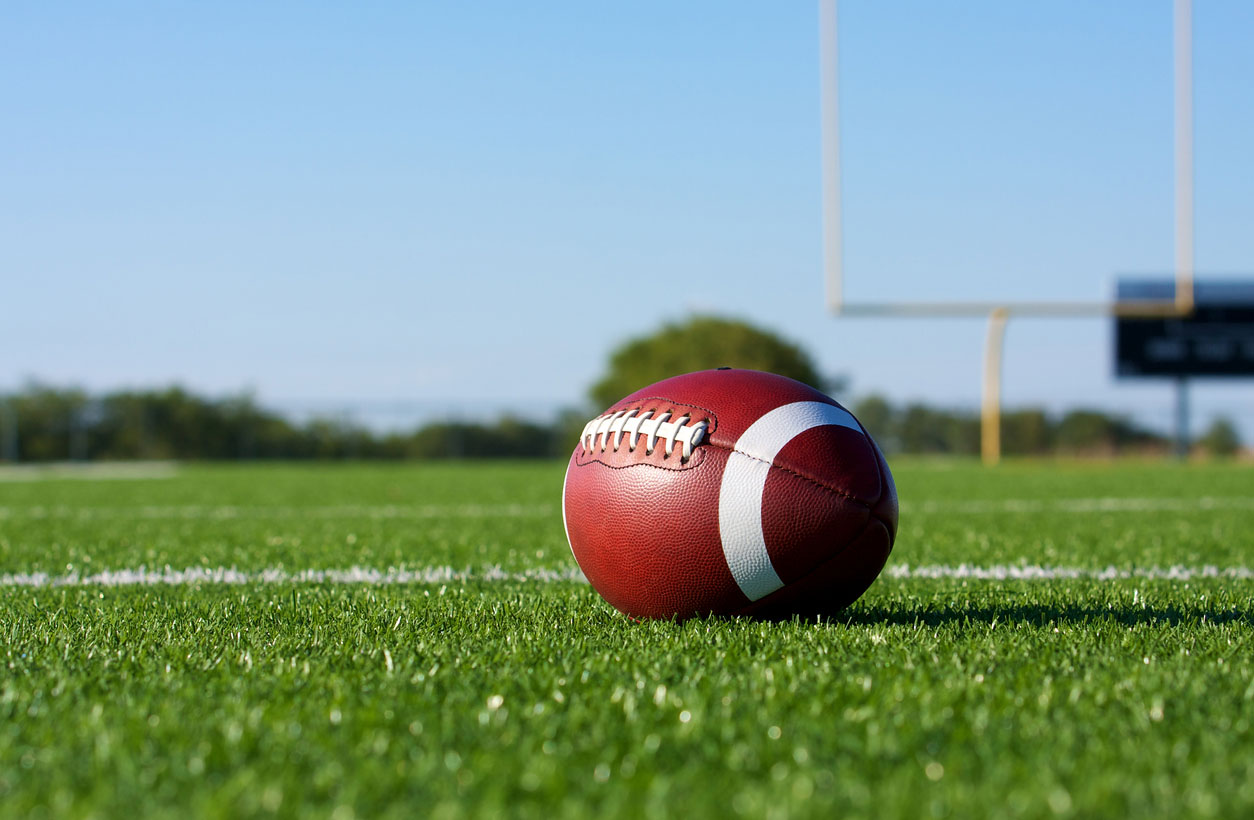 A football on turf with a football goal post in the background.