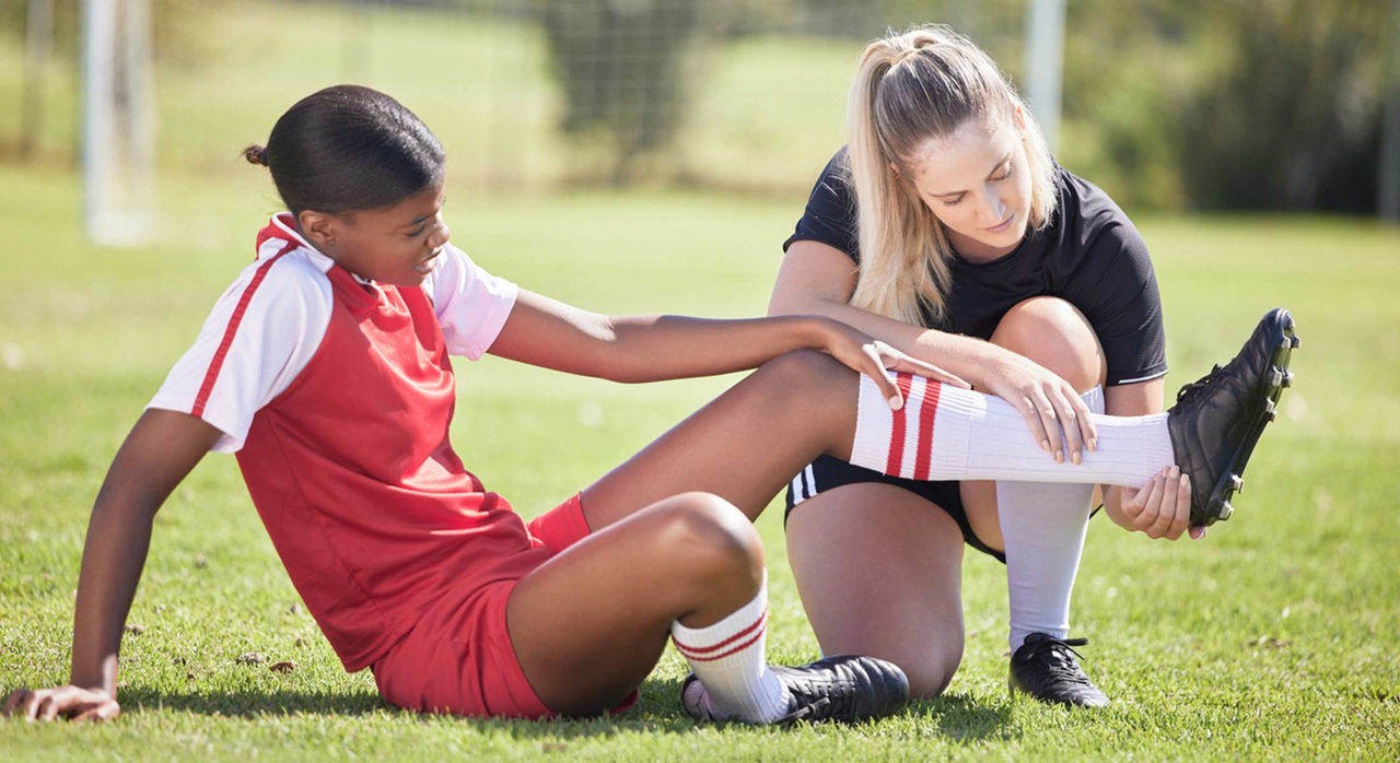 Female player with sore ankle on field being attended to by a sports medicine staff