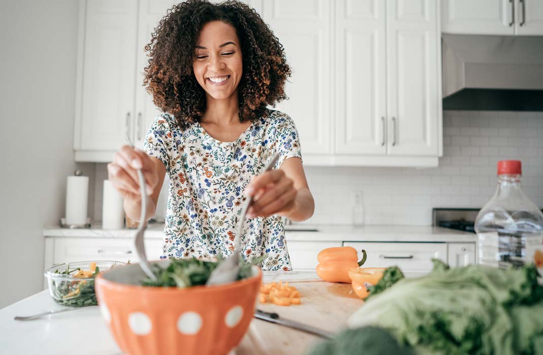 A woman in a floral top mixes salad in a kitchen
