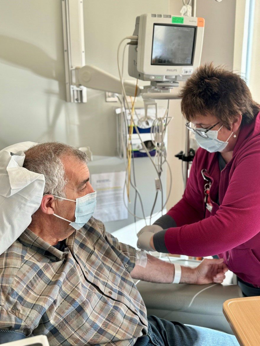 A provider injects medication into the IV line of a middle-aged man.