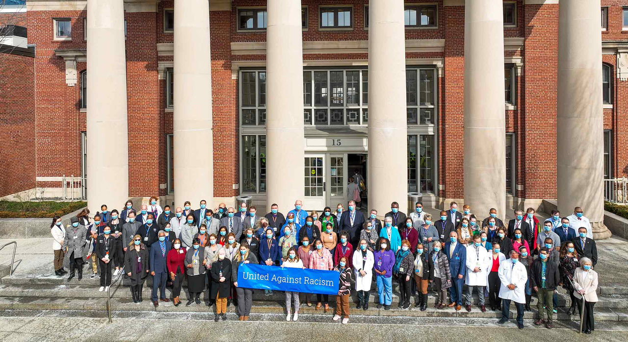 A group of people standing together holding a banner that says "United Against Racism"; Photo credit: Jim Rathmell