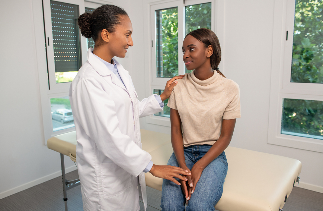 A patient sits on an exam table and talks to a nurse at an urgent care visit. 