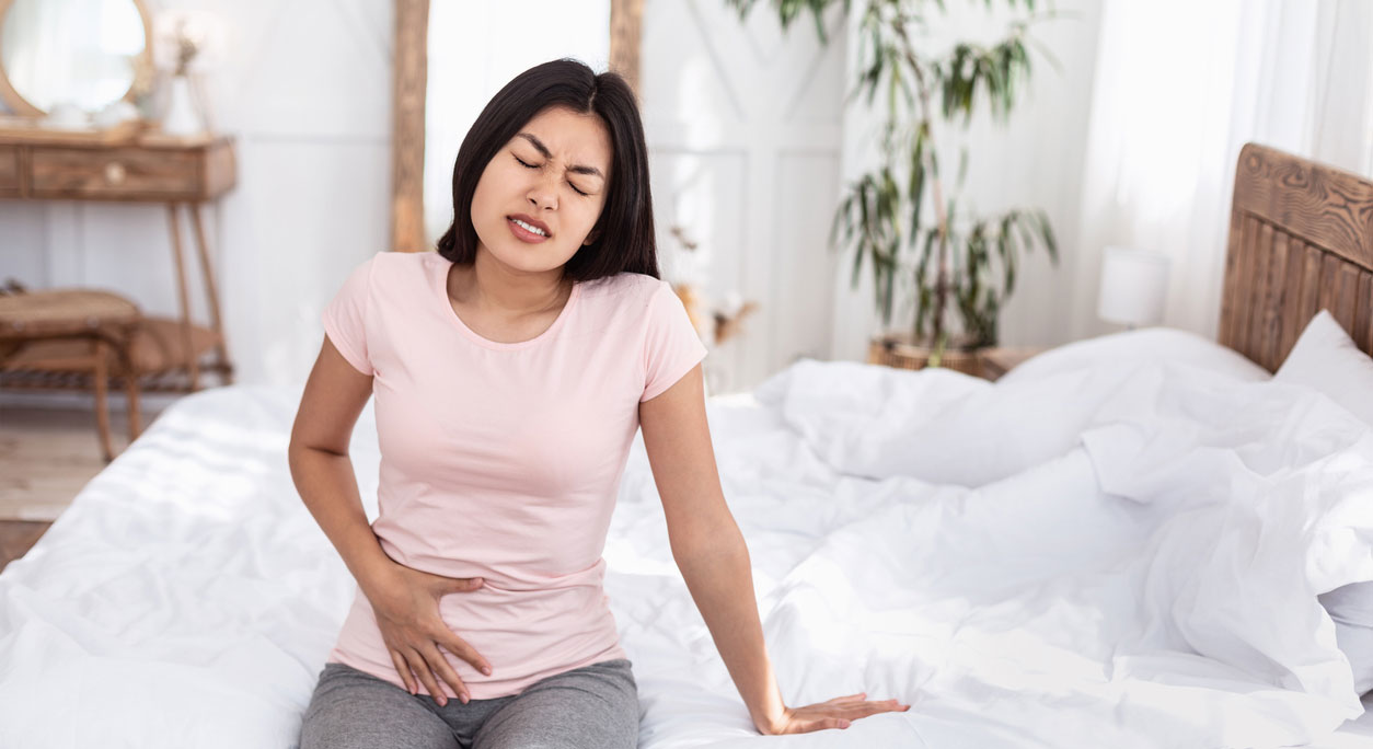 A young Asian-American woman clutches her lower stomach, grimacing in pain.
