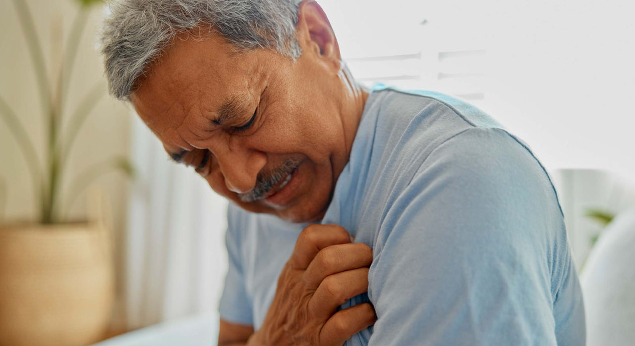 Man in a blue t-shirt clutches his chest while sitting on a white couch