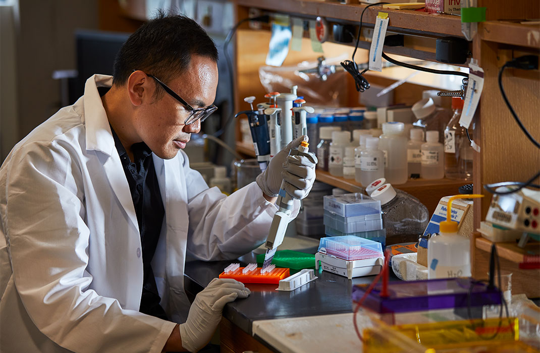 A researcher fills vials in a cluttered lab.