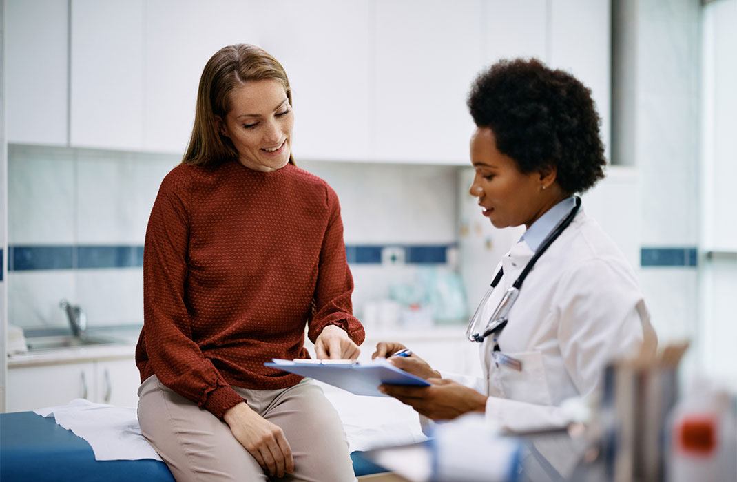 A female researcher interviews a woman in an examining room.