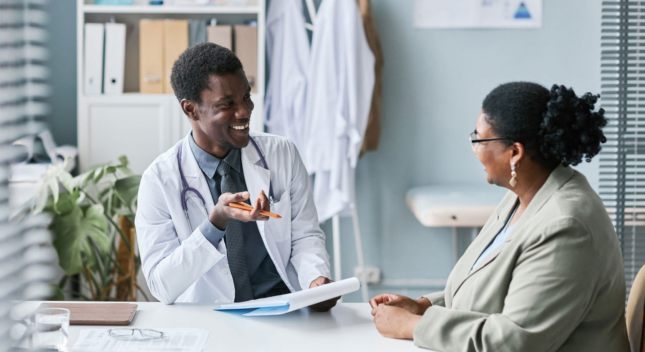A smiling male researcher interviews a female study subject in his office.