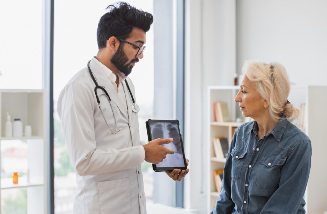 A doctor shows good chest scan results on tablet to a patient.