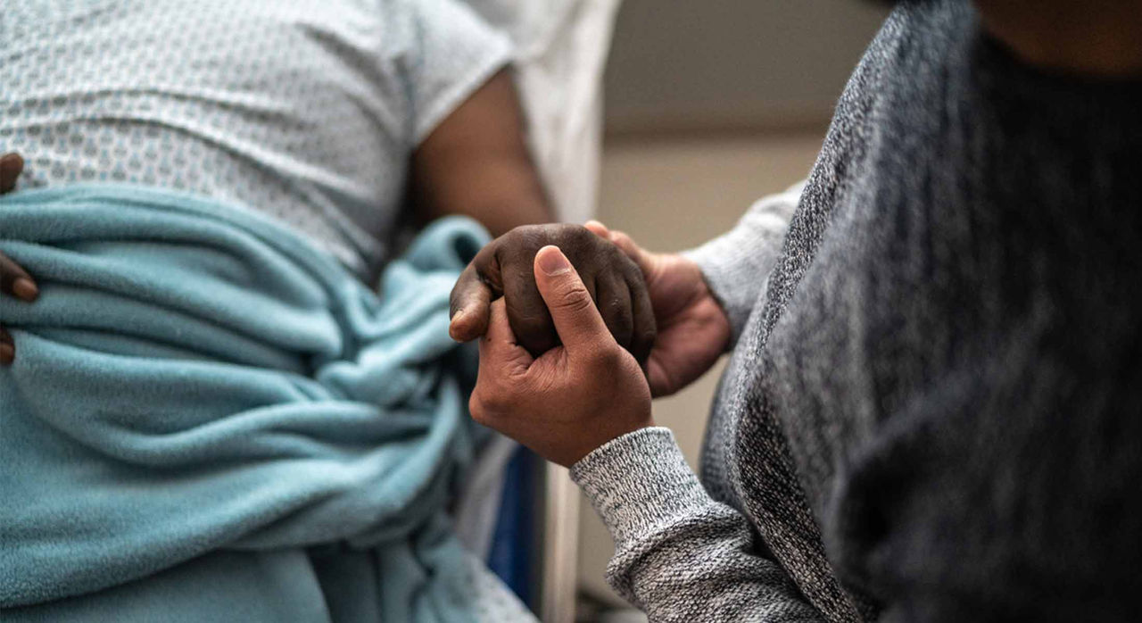 Patient on hospital bed holds hands with loved one