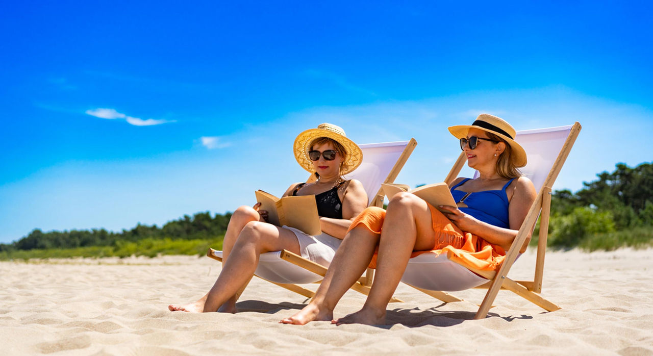Two women sit in chairs and read on the beach