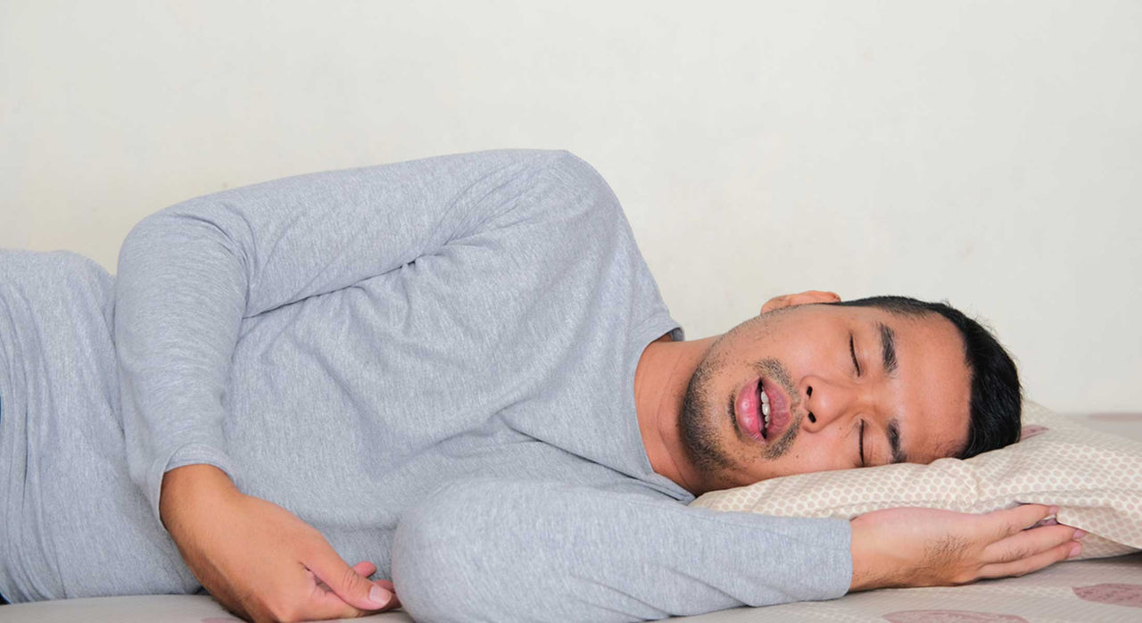 Man in a grey long-sleeve t-shirt sleeping with mouth open.