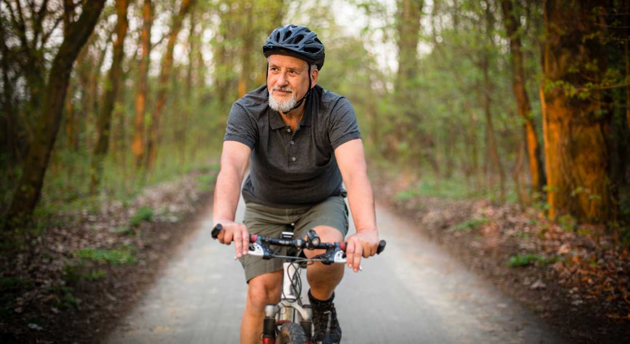 An older man riding a bicycle on a wooded bike path.