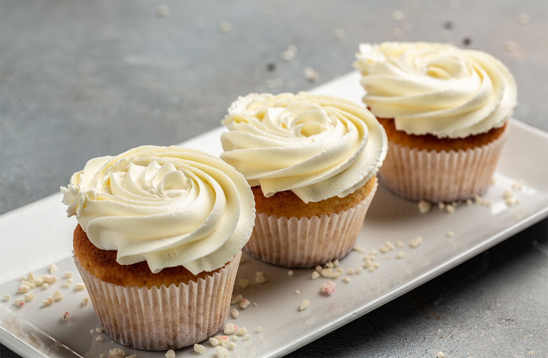Three frosted vanilla cupcakes on a plate.