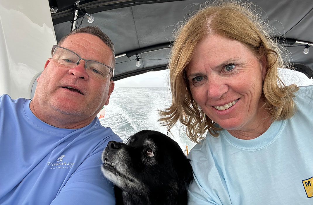 A middle-aged white couple and their little black dog aboard a boat.