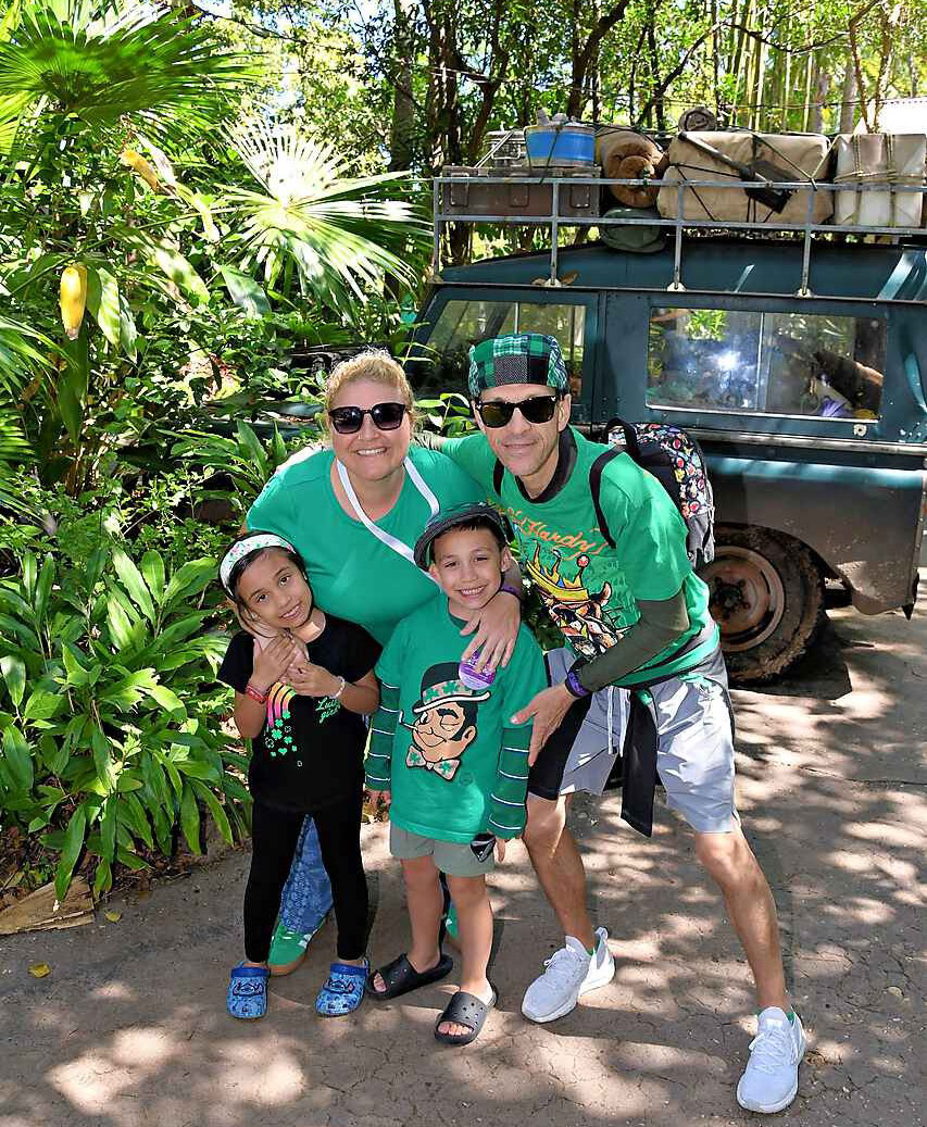 Brandon, his sister, and his parents pose in the jungle, with a Jeep loaded with camping supplies in the background.
