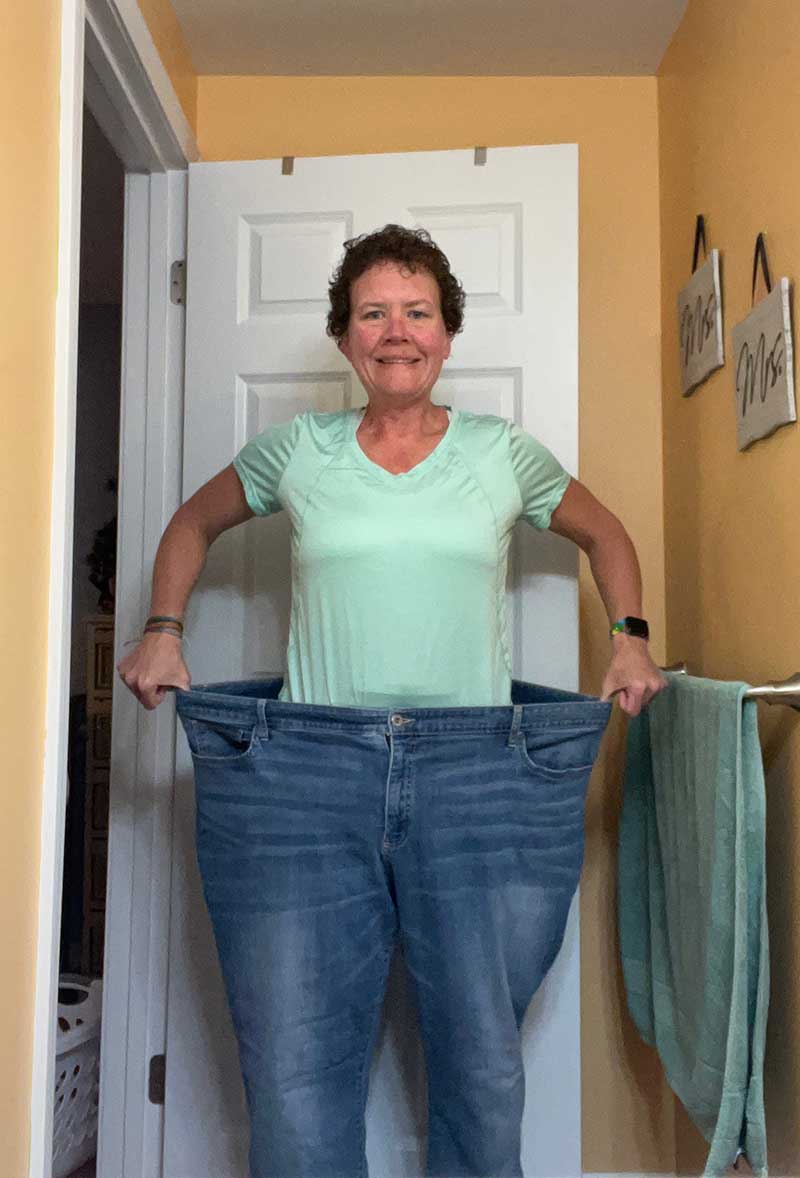 Carrie wears her pre-weight-loss pants, pulling the waistband out to show how big they are on her body.