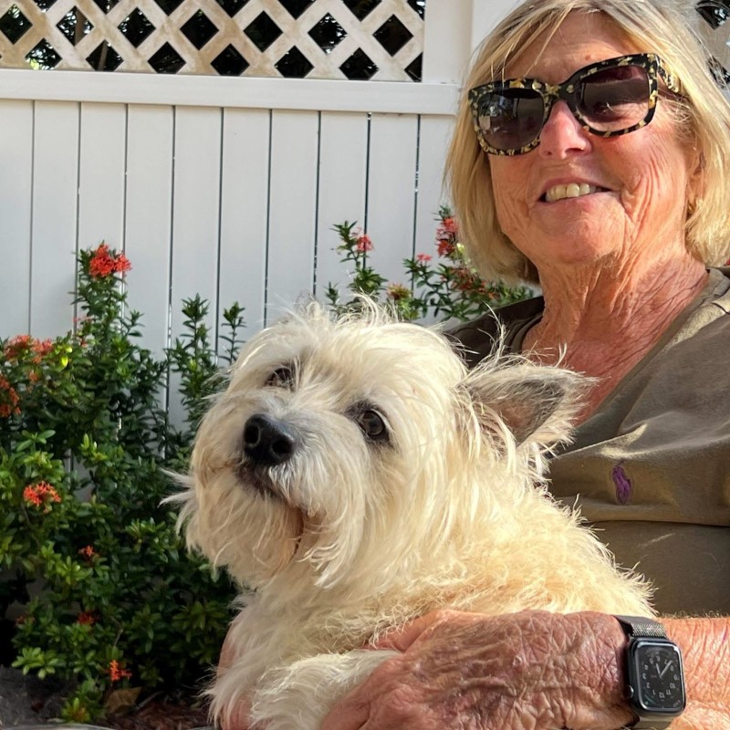 Woman wearing sunglasses smiling holding a small white dog