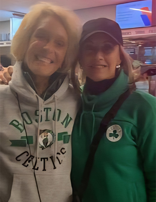 Two women wearing Boston Celtics-themed hoodies are seen in a casual indoor environment.