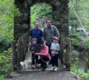 A family of five poses on a wooden bridge surrounded by lush greenery.