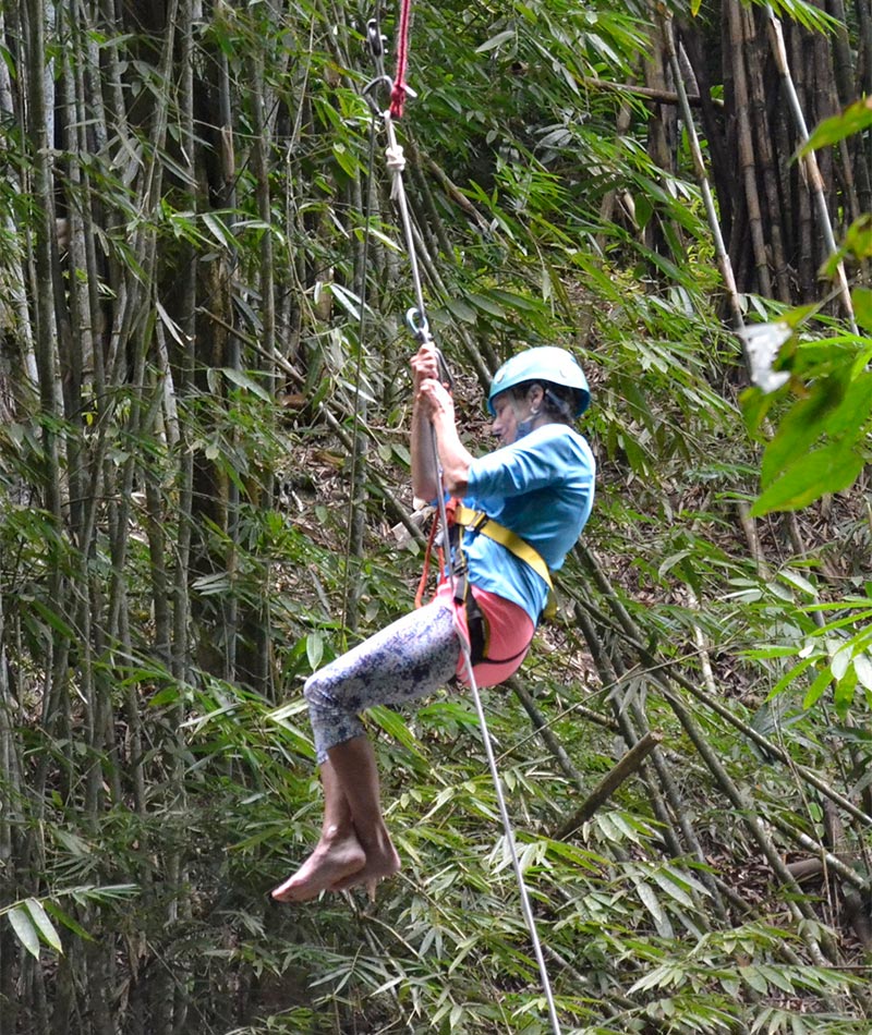 A woman wearing a helmet and harness is rappelling down amidst a dense forest.